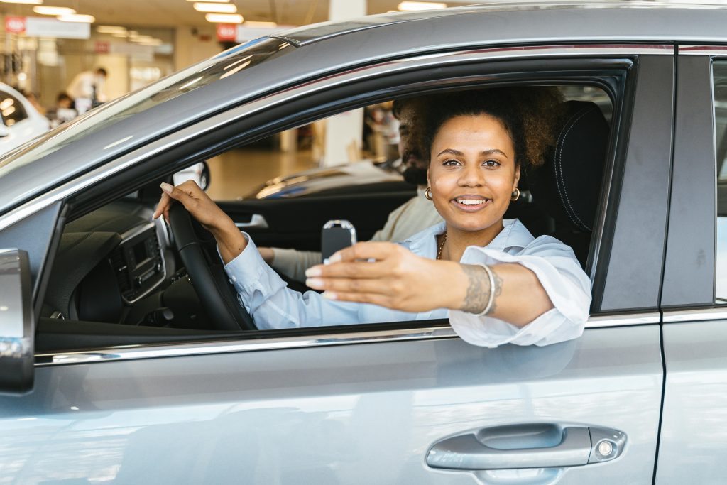 Woman sitting in the drivers seat of her car with her arm out of the window holding the car key